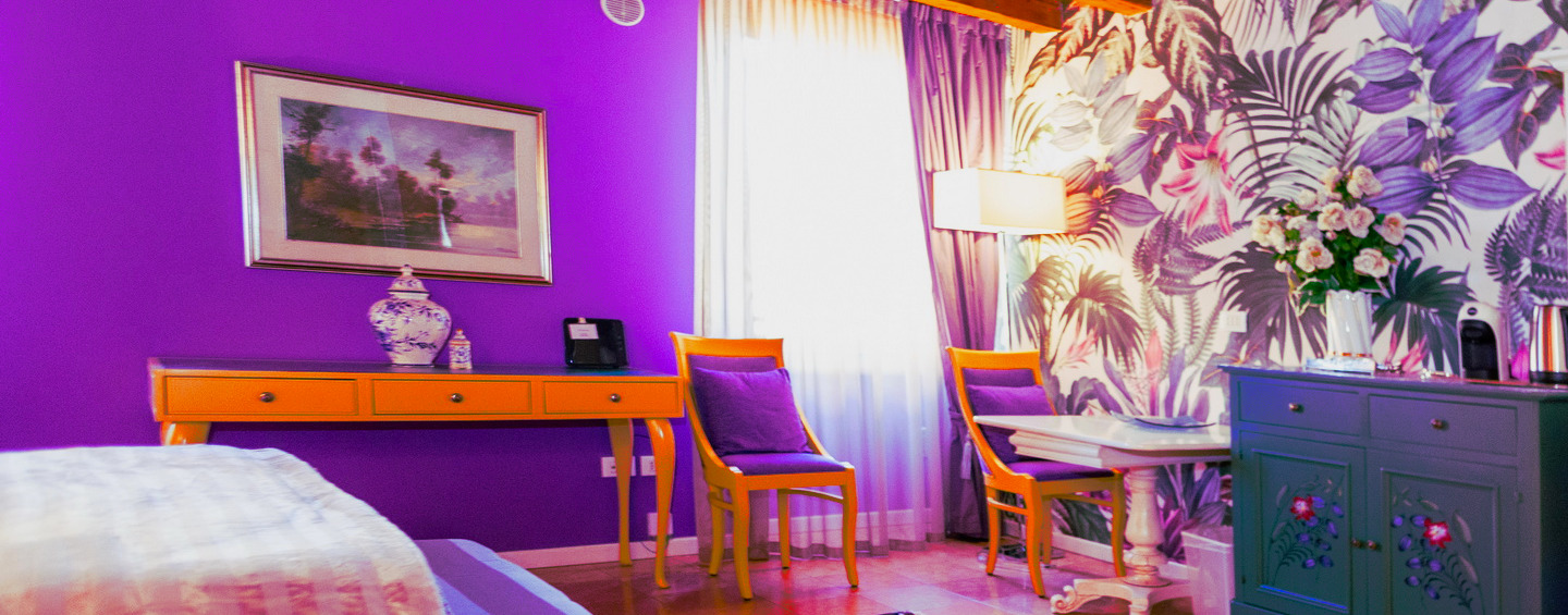 a picture of the room, bed with blank and pillow, purple wall with a paint hanged